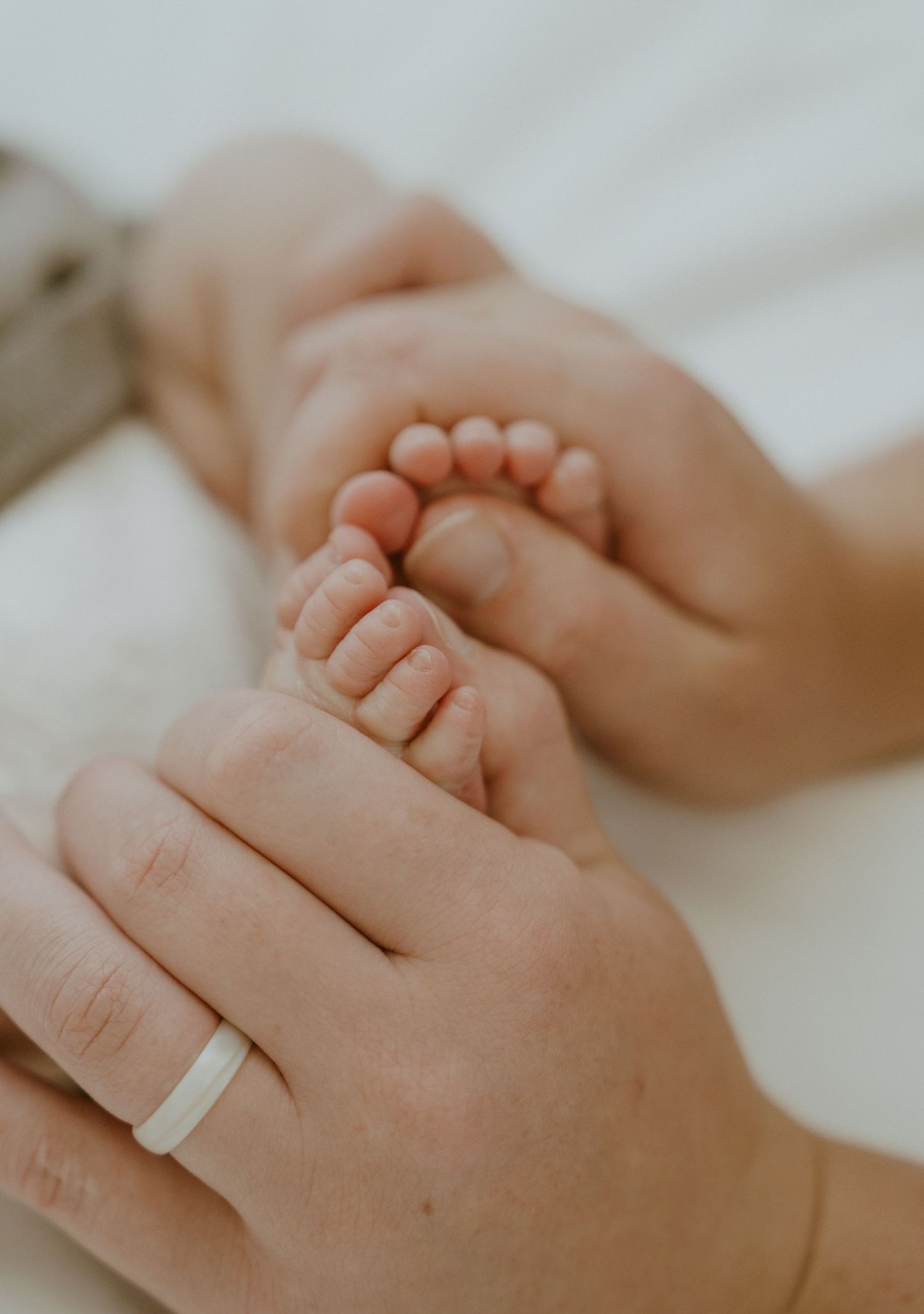 Close-up of tiny baby feet being held by adult hands with a white ring.