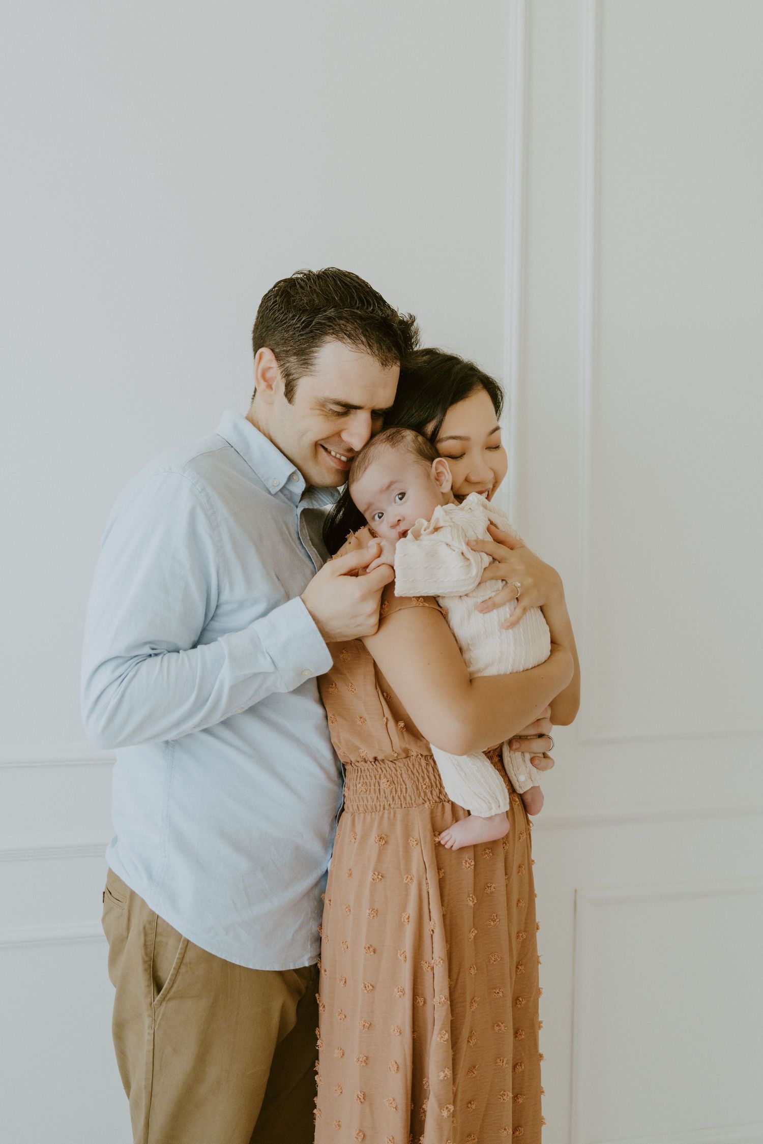 An intimate family portrait sharing joyful moment with their baby against white wall.
