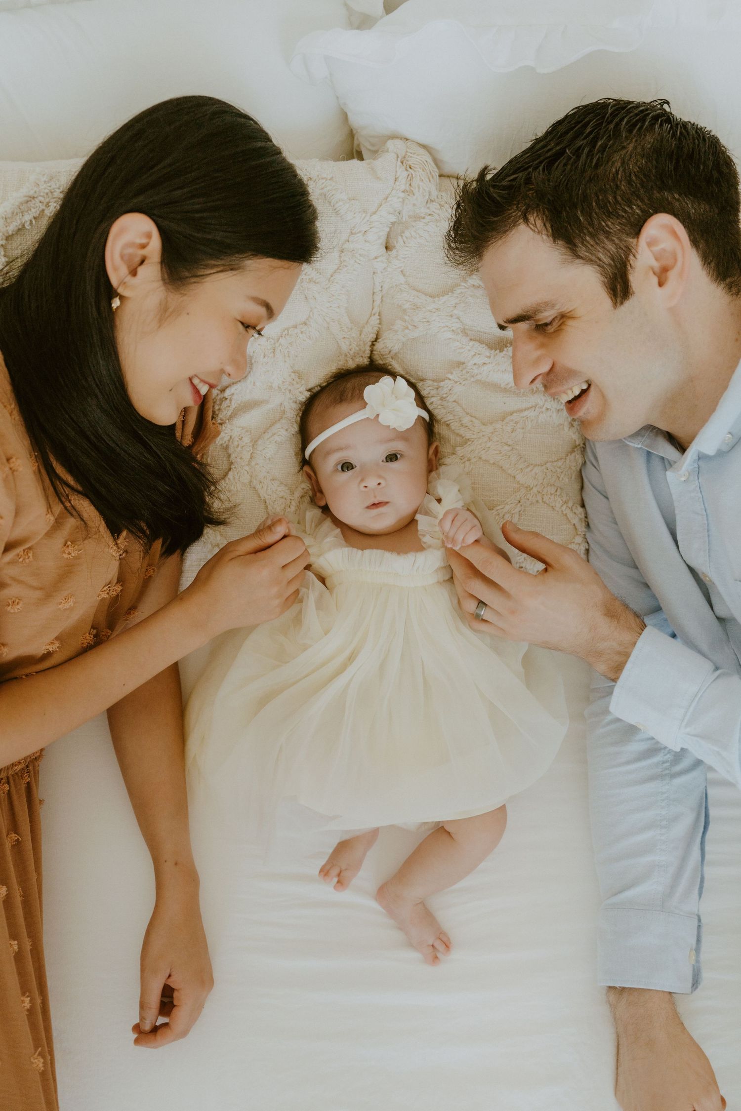 A family lying on white bedding sharing an intimate moment with their infant.