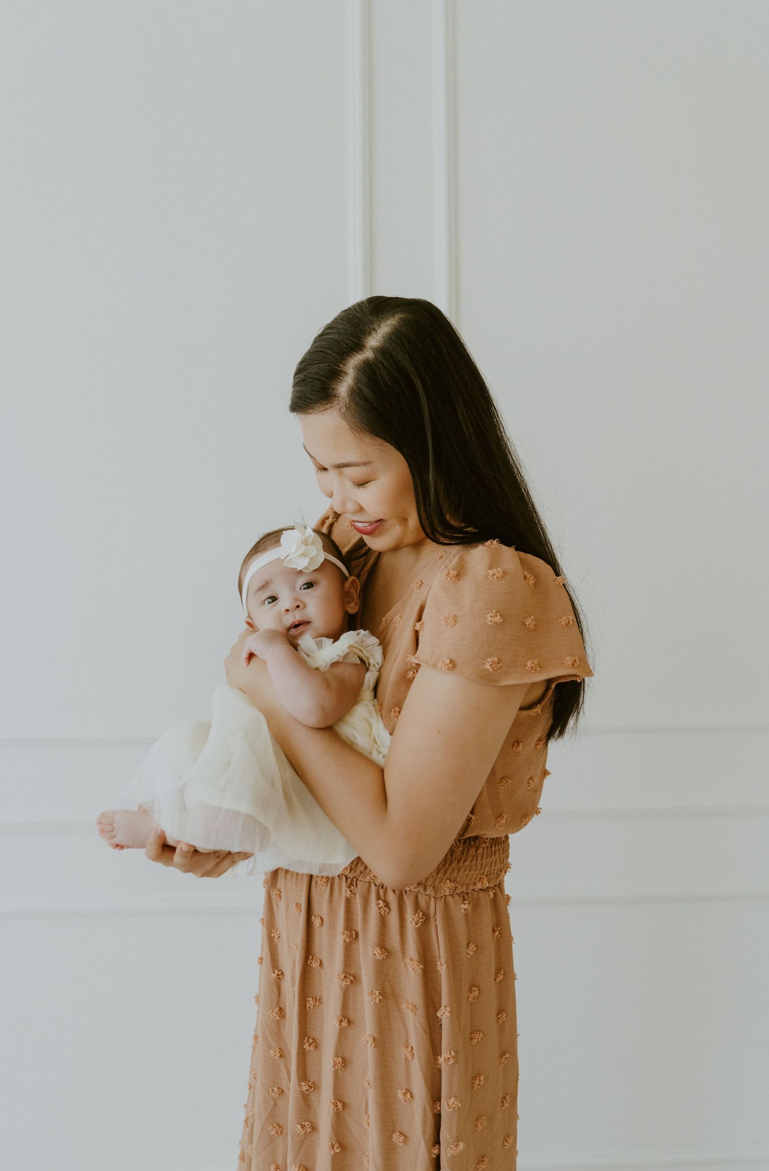 A tender moment between parent and baby in white against minimalist backdrop.