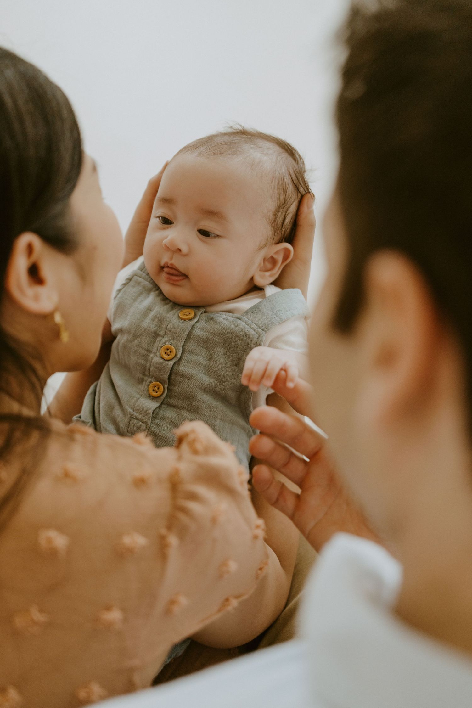 A tender family moment with an infant in gray clothing being held lovingly.