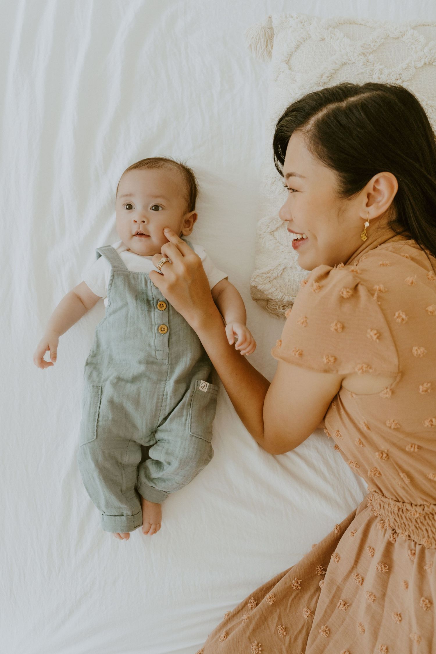 A joyful moment between parent and baby lying on white bedding.