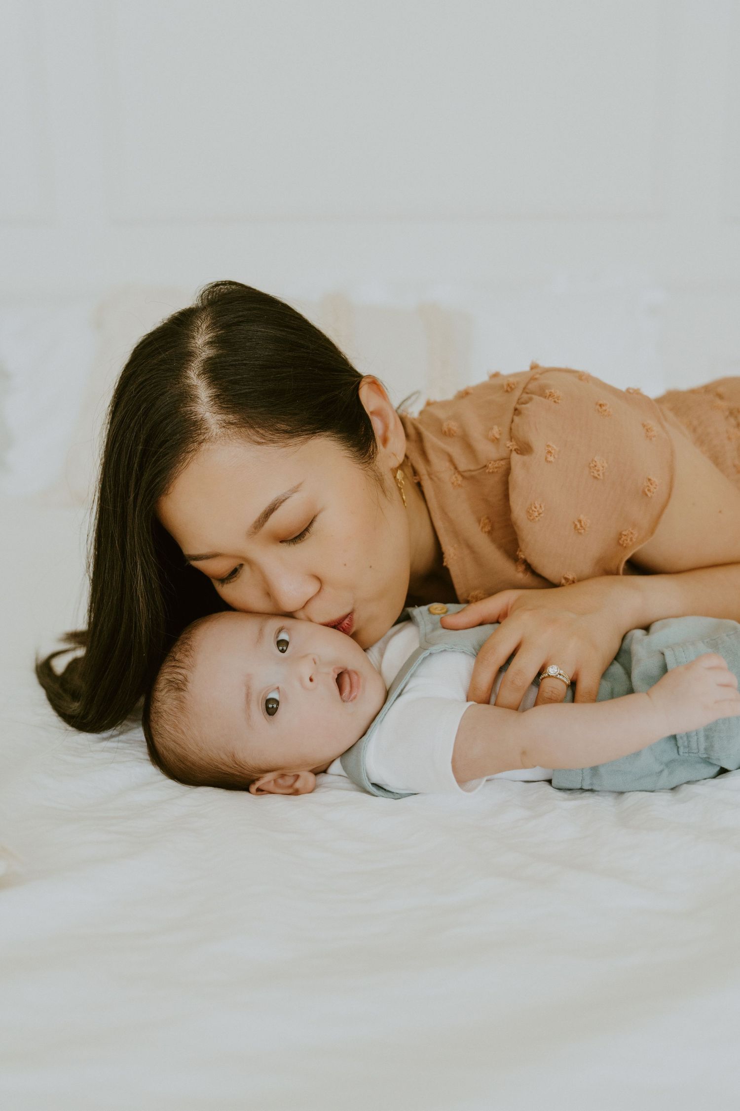 An intimate moment between parent and baby lying together on white bedding.