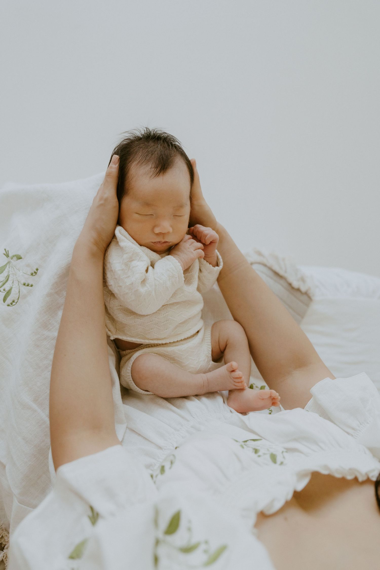 Sleeping baby in white clothing lying on white textured bedding.