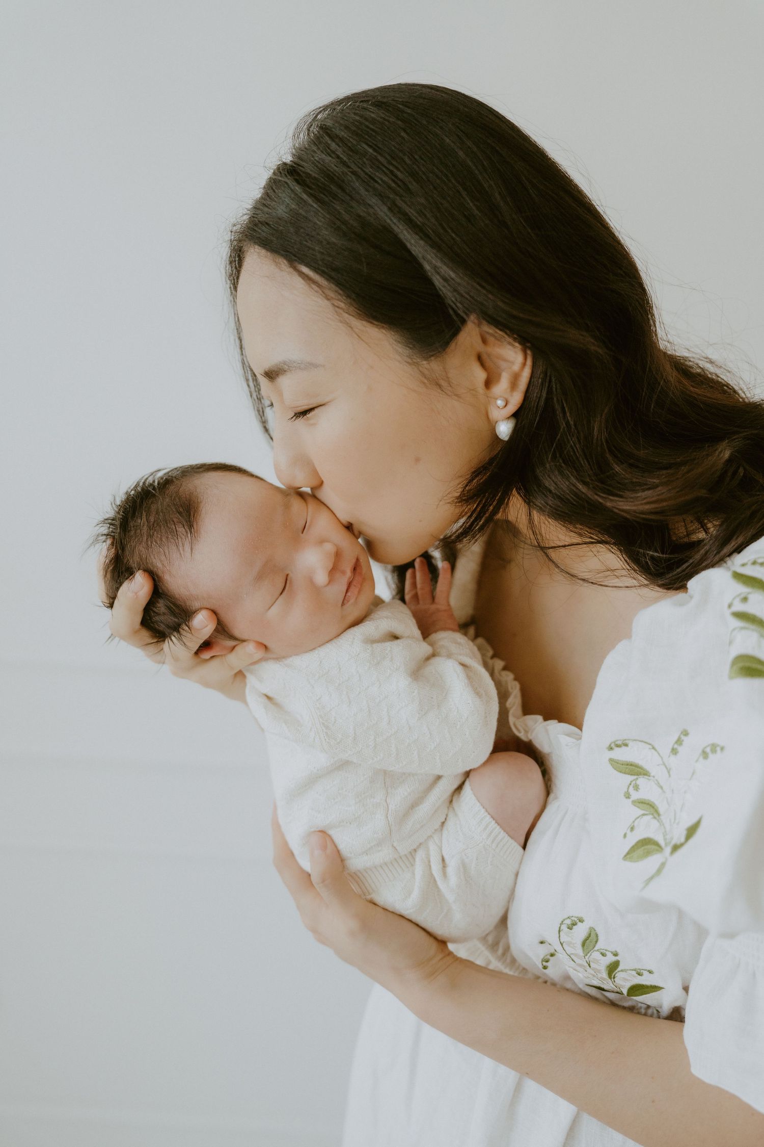 Tender moment between parent and sleeping newborn against white background.