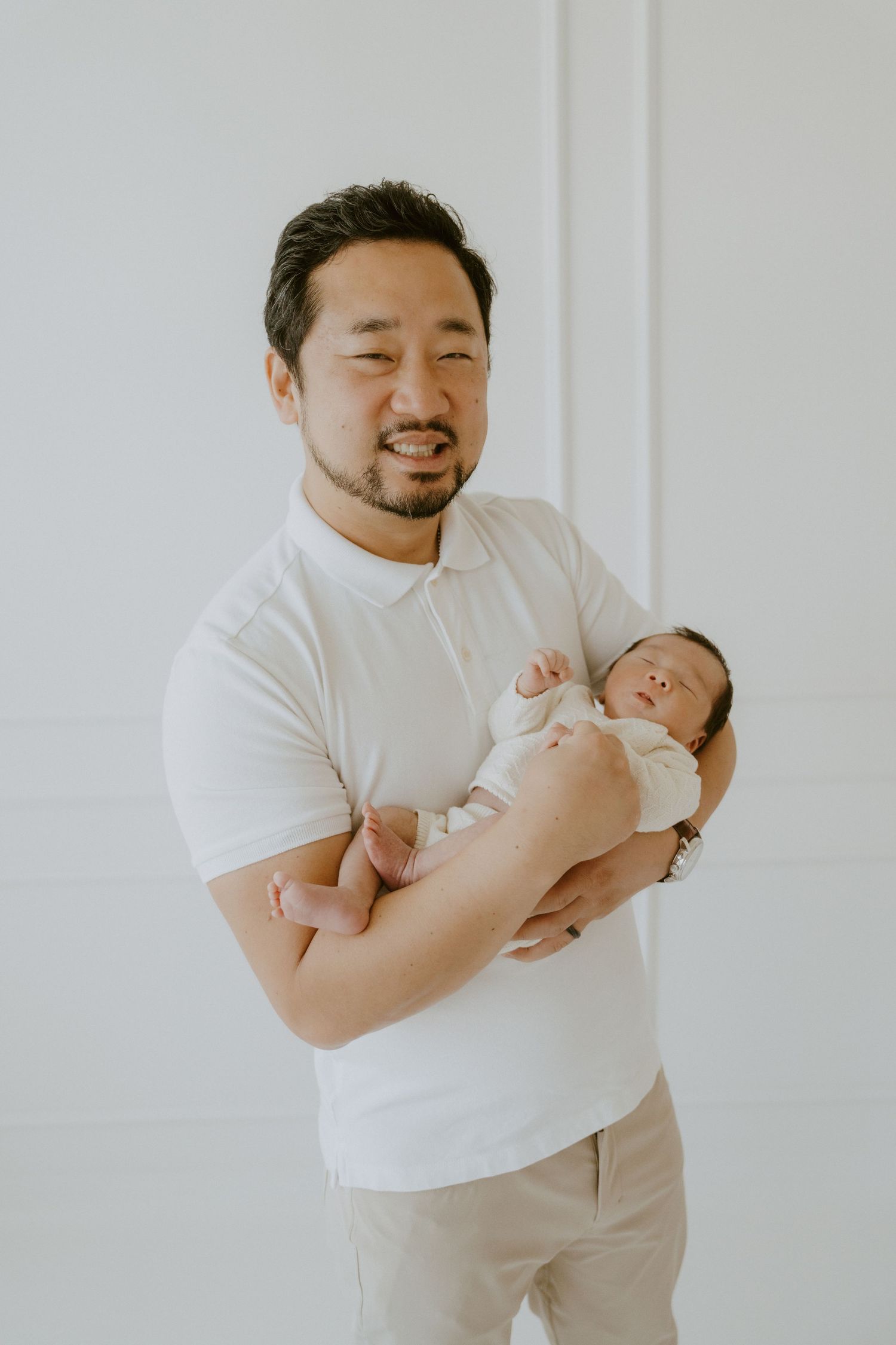 A person in a white shirt holds and gazes lovingly at a sleeping newborn baby.