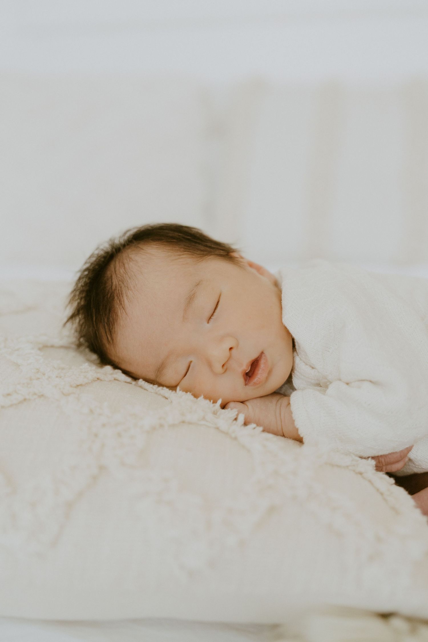 Peaceful sleeping newborn wrapped in white blanket.