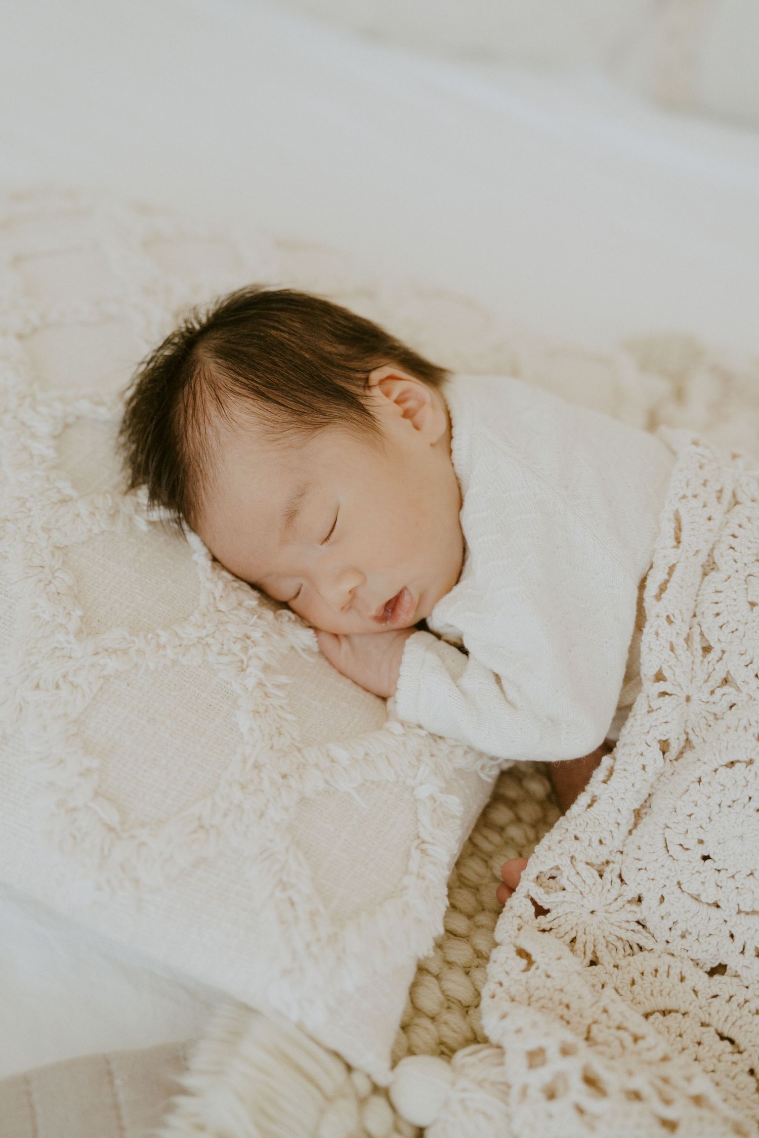 A sleeping newborn baby wrapped in white lace blankets.