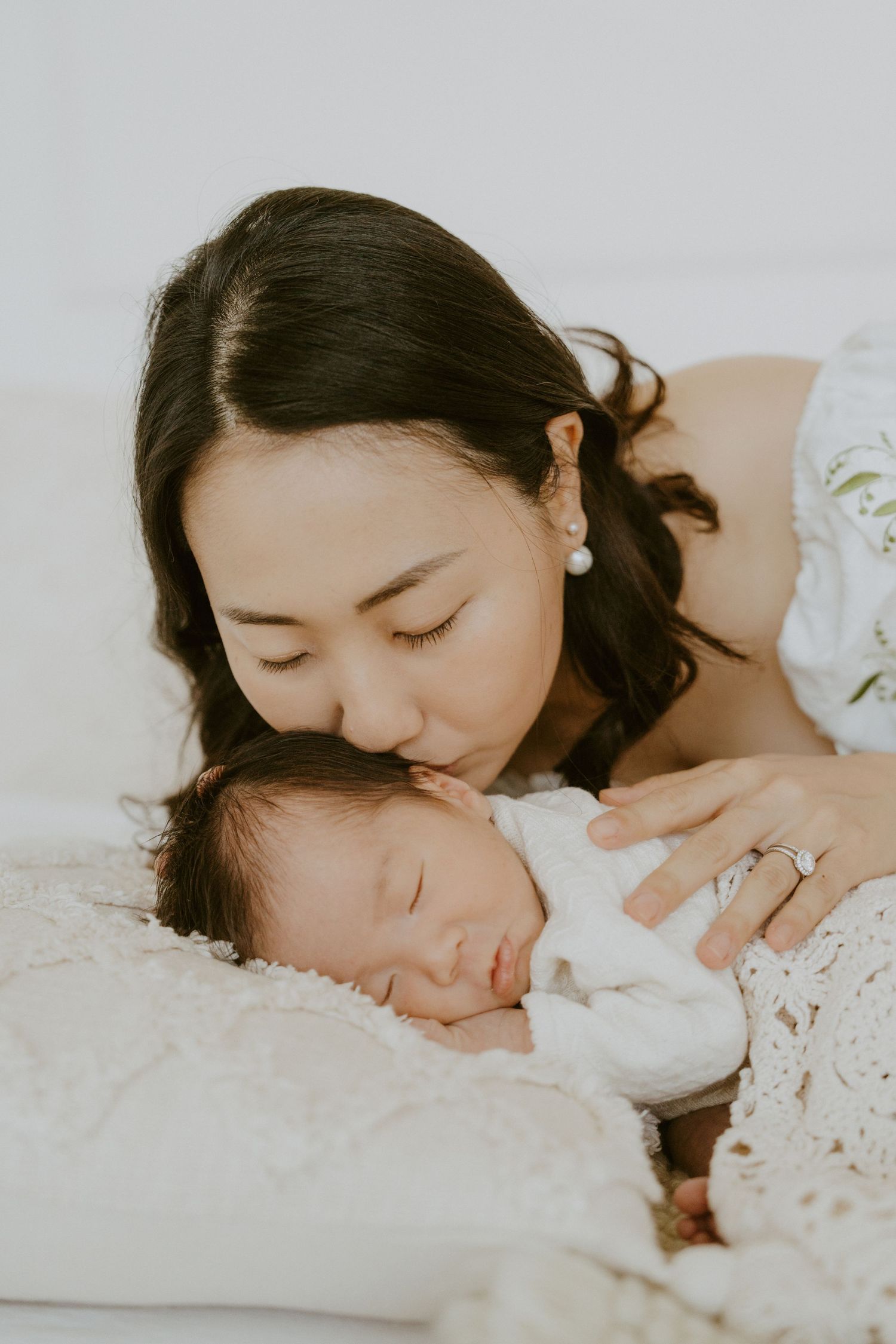 Parent kissing sleeping newborn on soft white bedding.