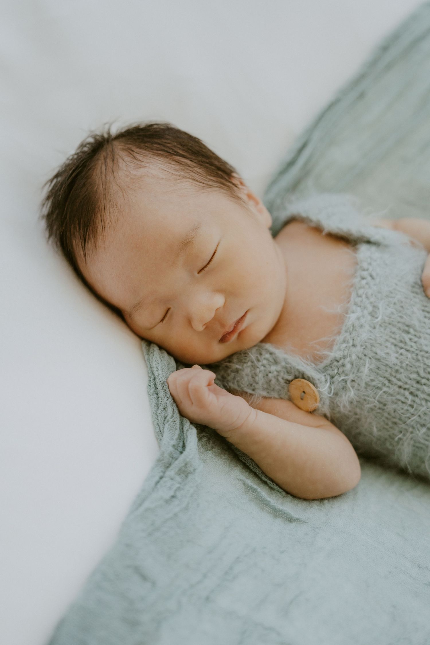 Sleeping infant wearing gray knit clothing rests peacefully on soft blanket.
