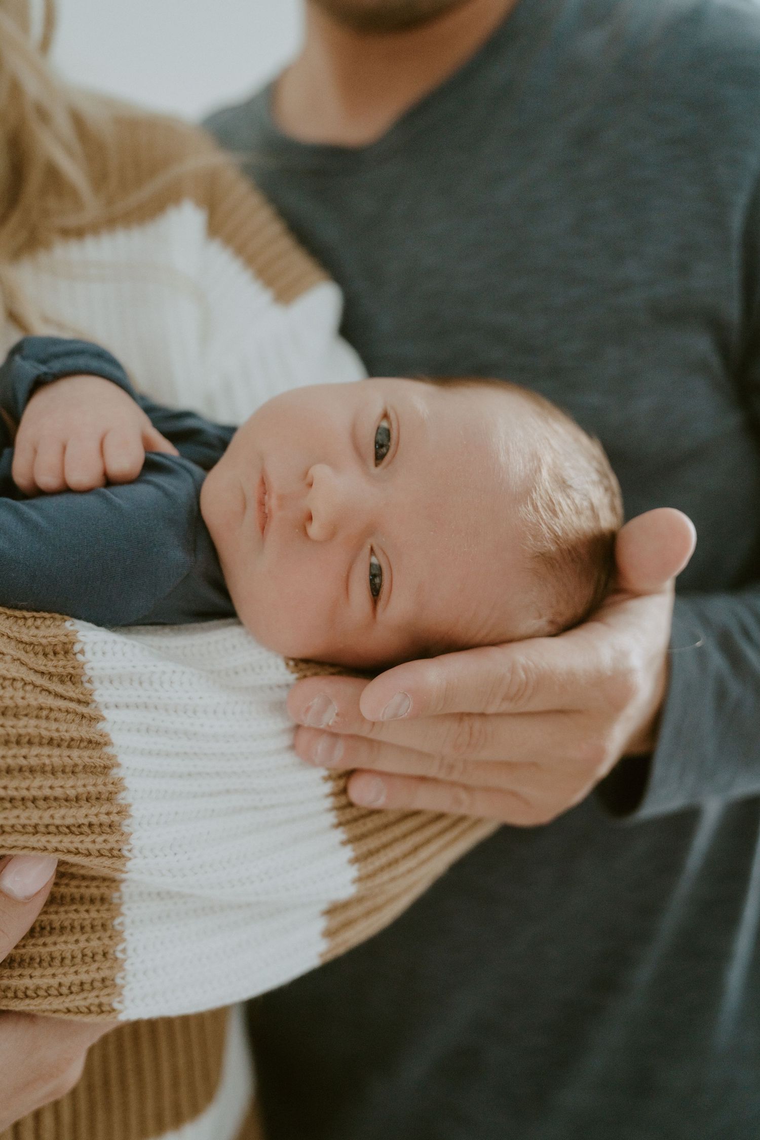 Close up of an alert newborn baby with bright eyes being cradled gently.