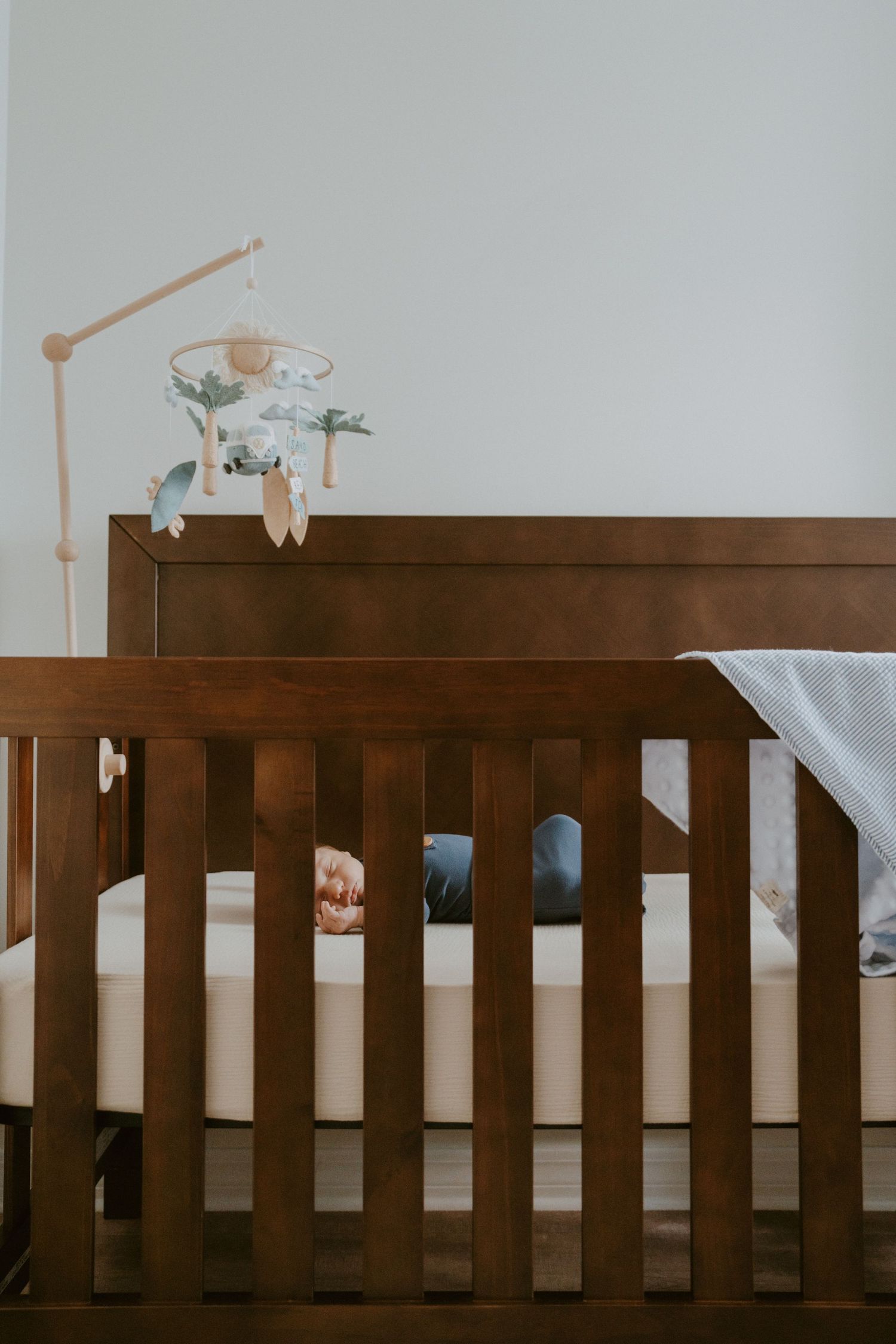 Wooden crib with mobile in minimalist nursery with white walls.