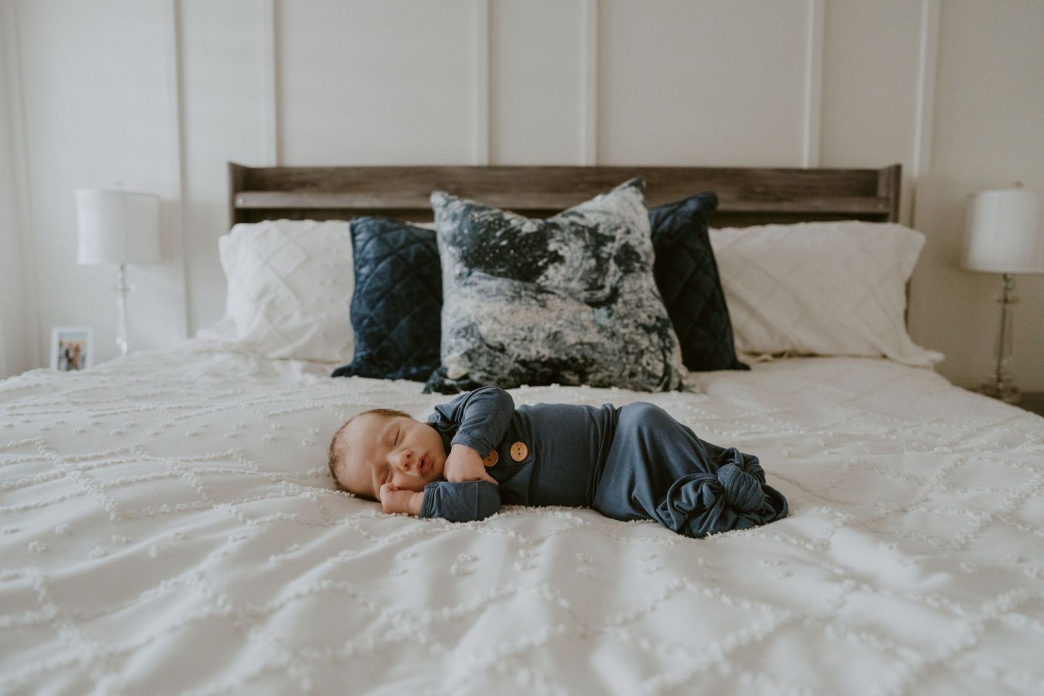Baby in navy outfit sleeping peacefully on white bedding.