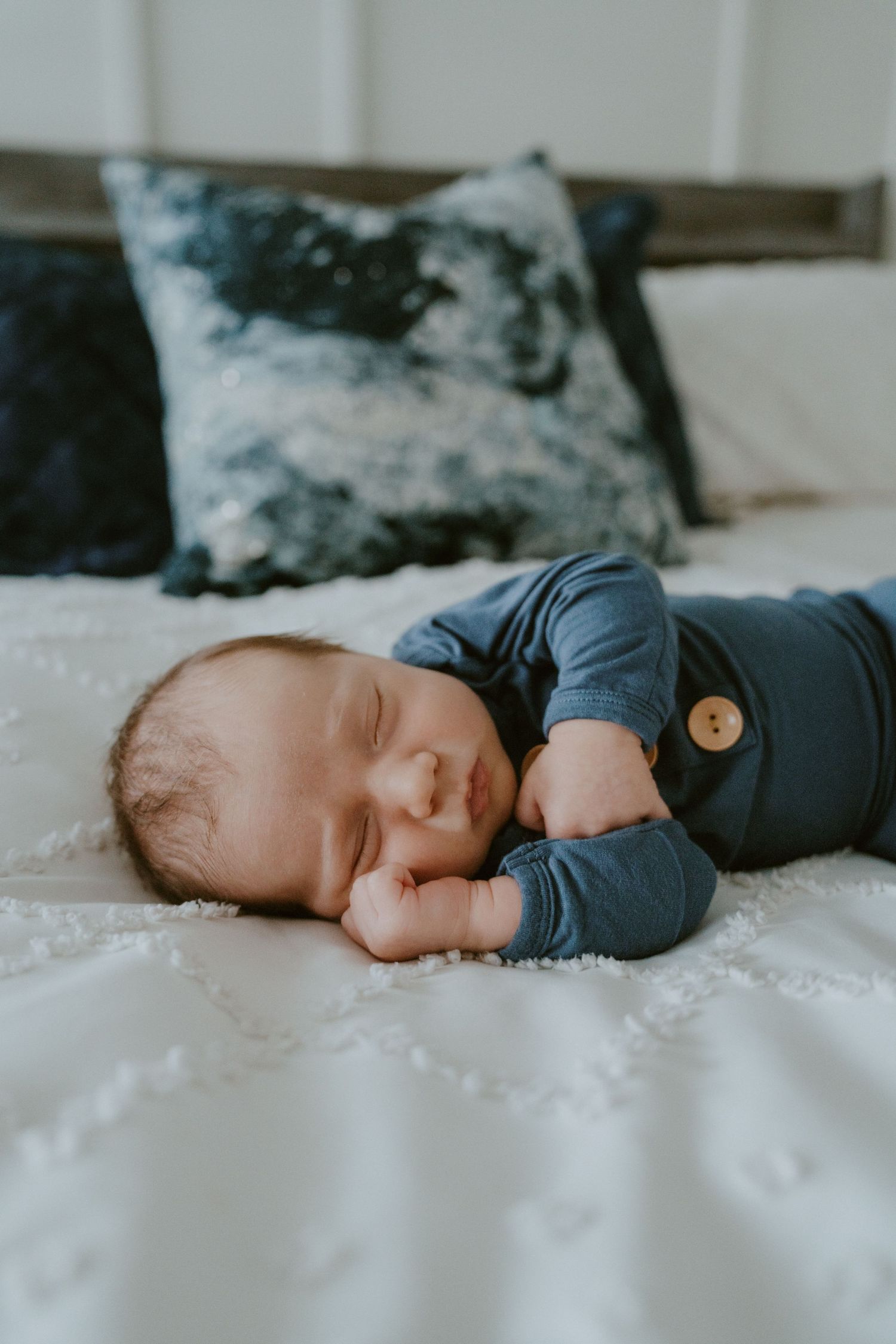 Baby napping on white bed with decorative pillows in background.