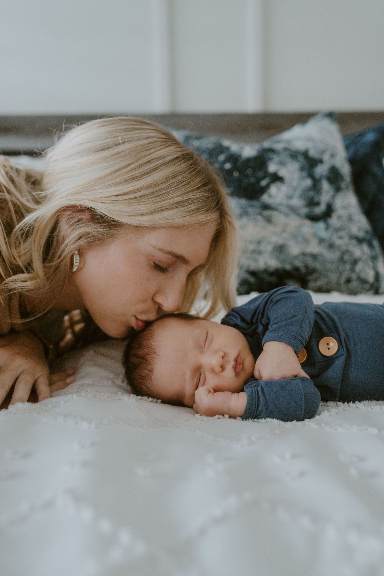 Tender moment between parent and sleeping infant on white bedding.
