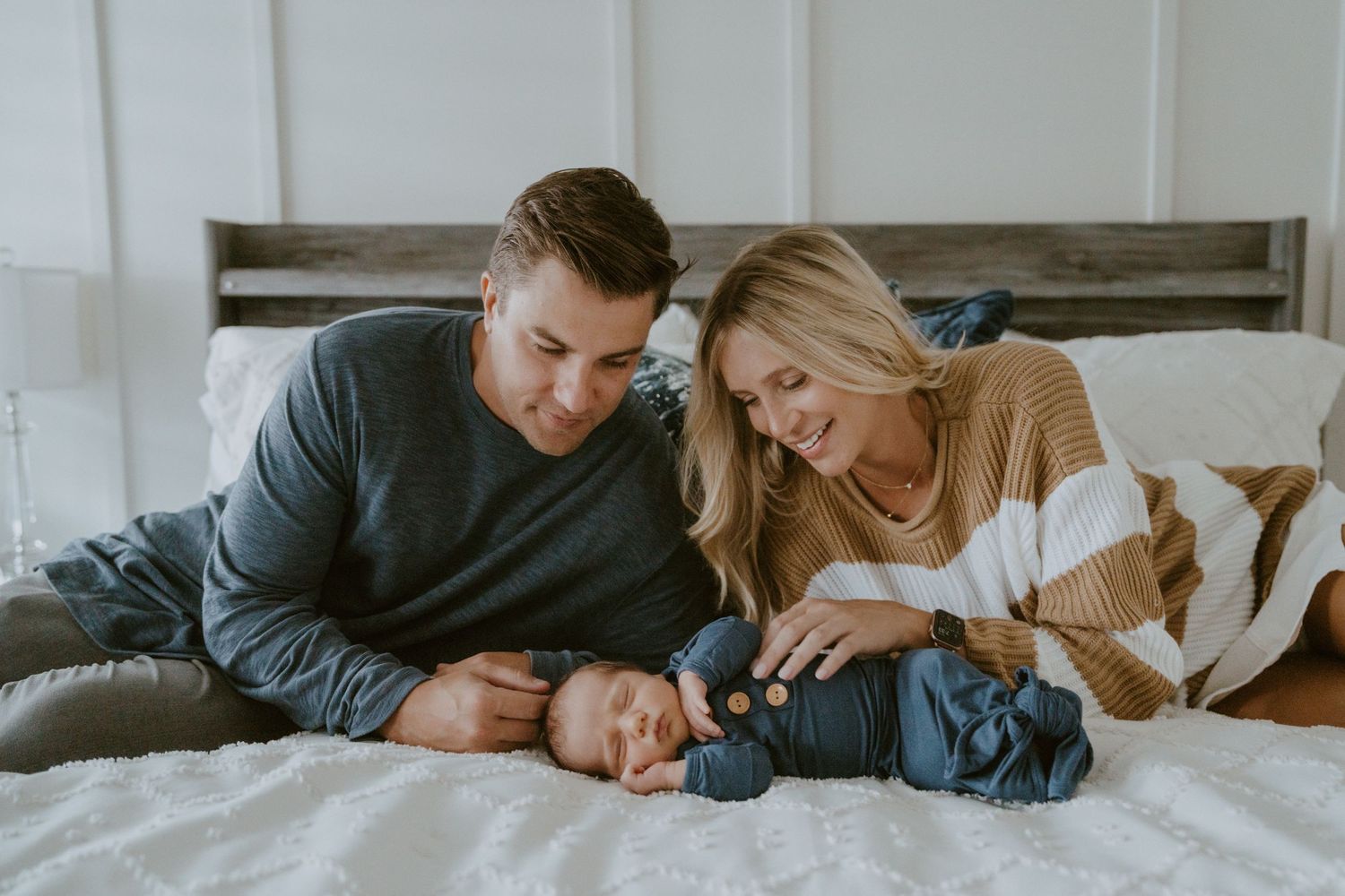 Intimate family moment on white bed with wooden headboard.