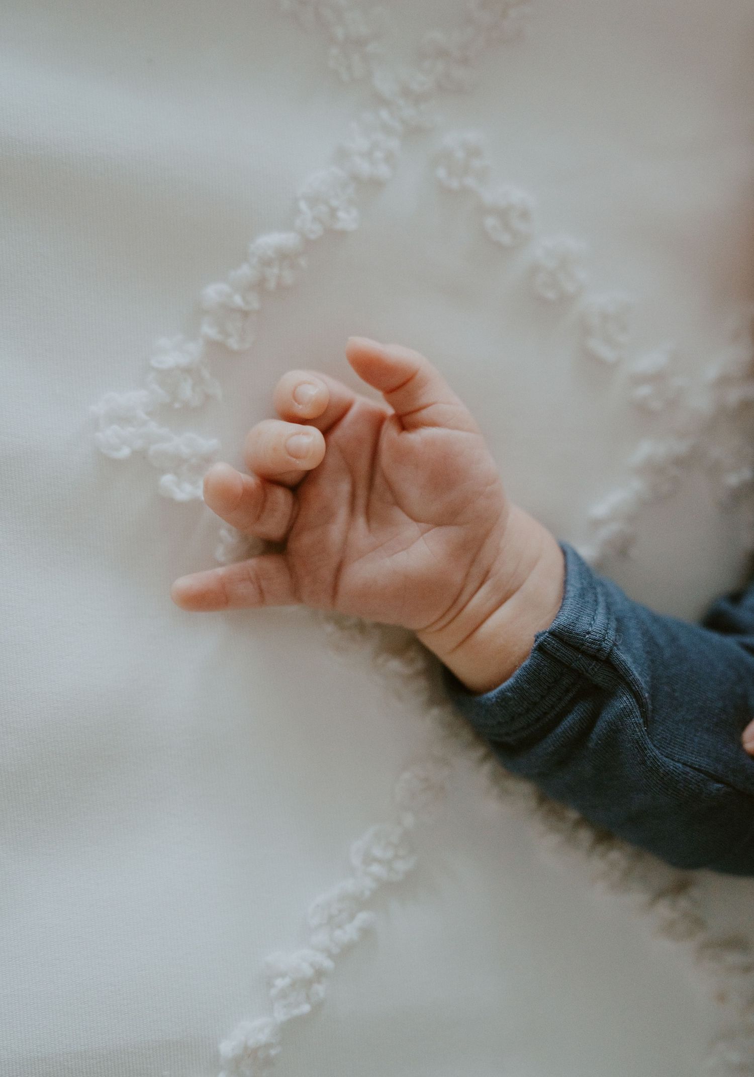Tiny baby hand resting on white textured fabric.
