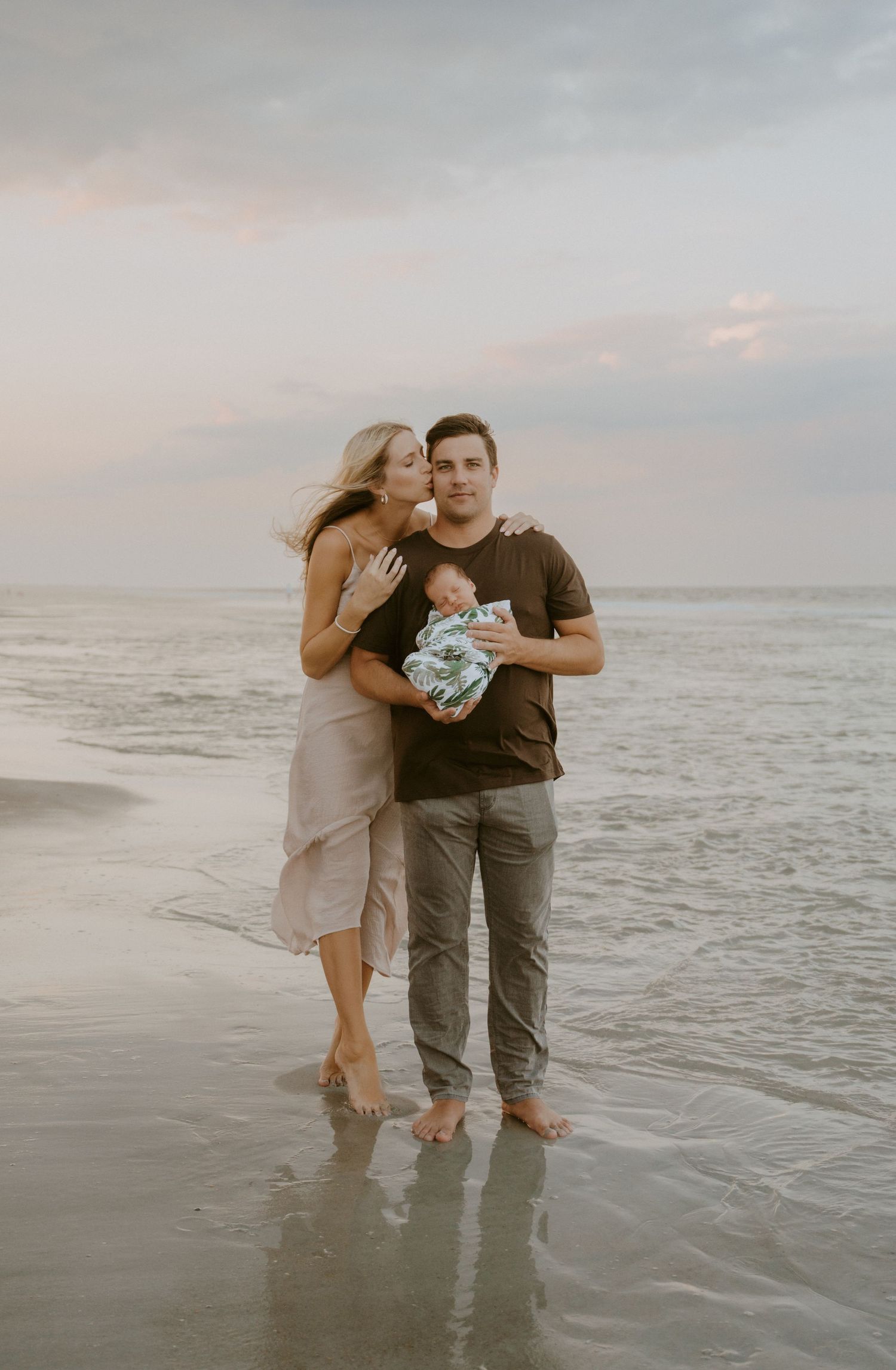 Family standing together on beach at sunset with waves in background.