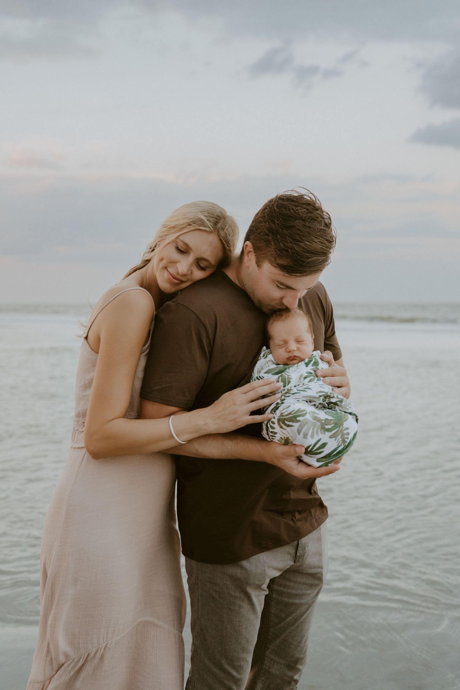 Intimate family moment on beach during golden hour with ocean backdrop.