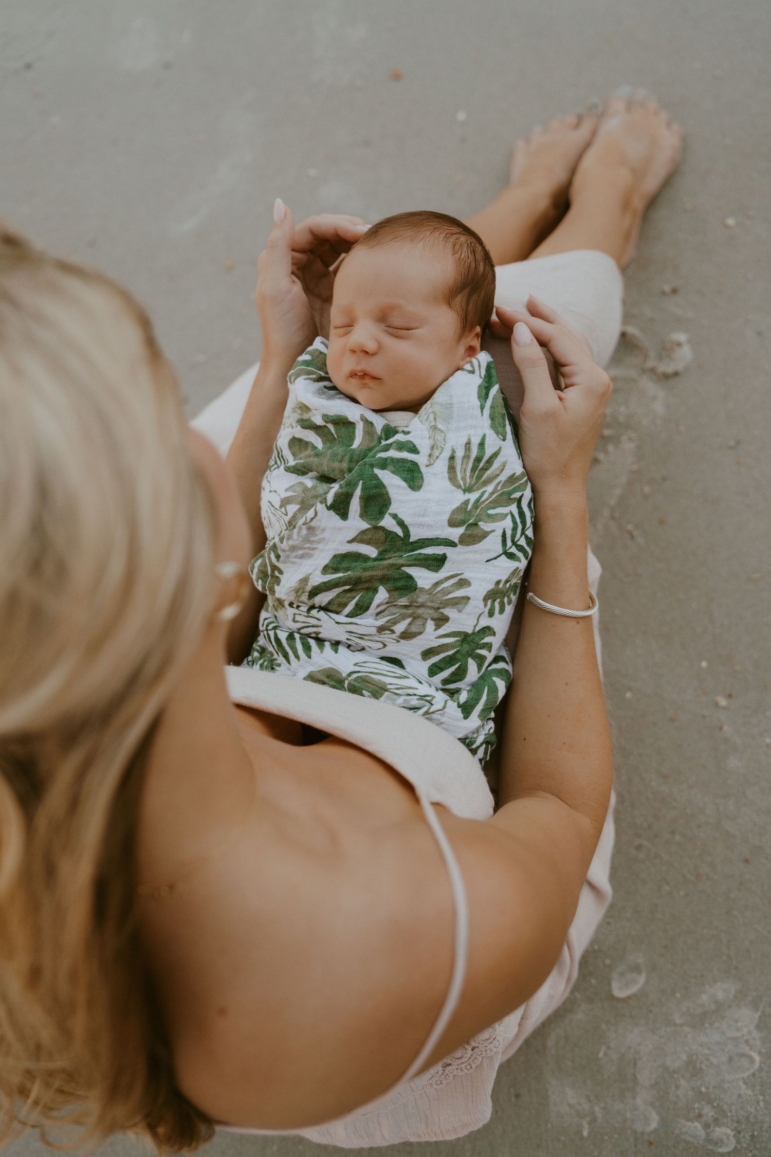 Sleeping infant wearing tropical leaf print outfit rests peacefully against caregiver.
