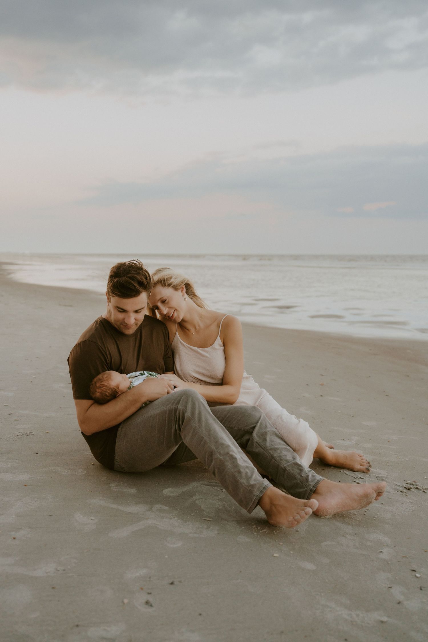 Couple sits together on sandy beach at sunset sharing intimate moment.