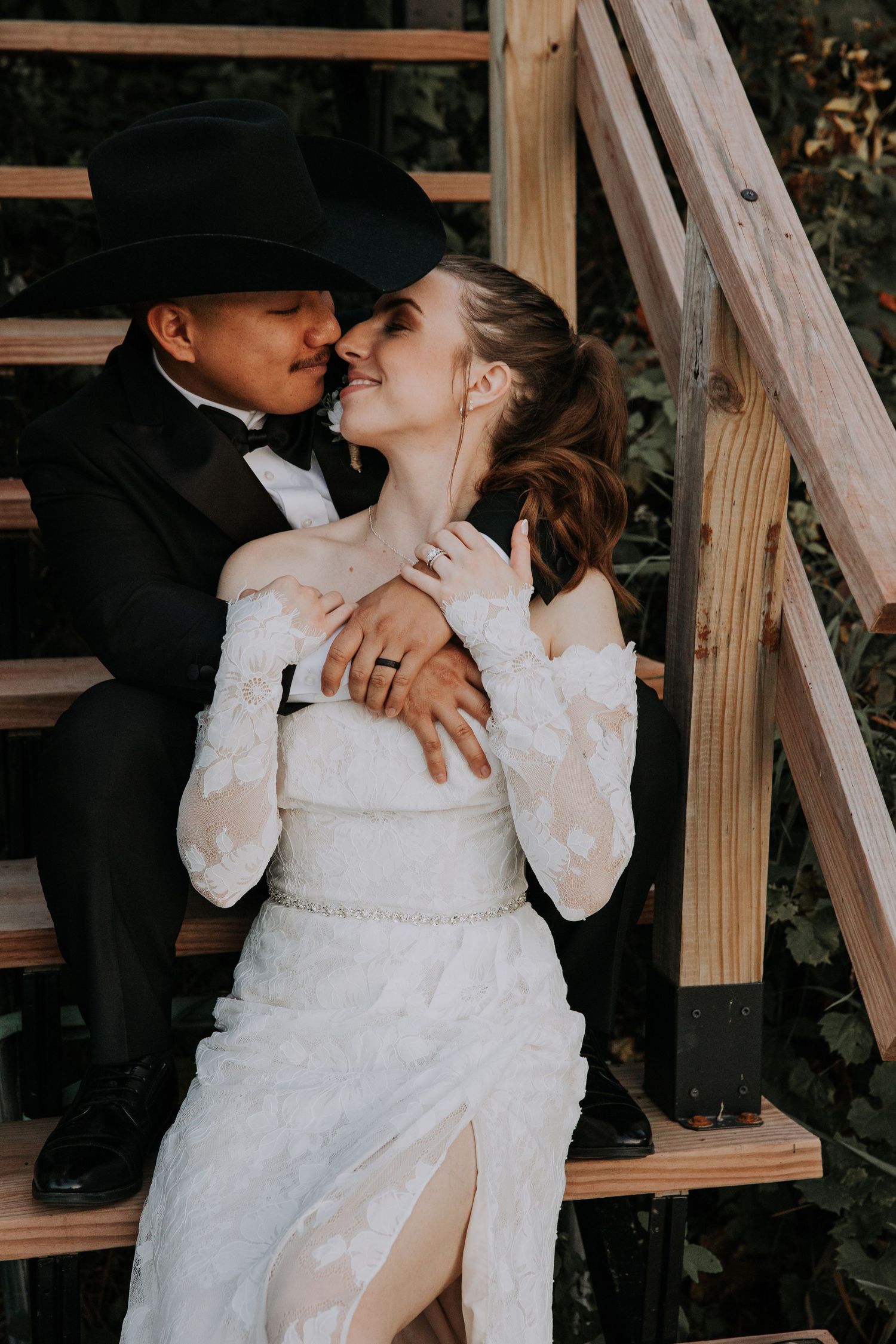 A romantic wedding couple embracing on grassy grounds beside a winding river under cloudy skies.