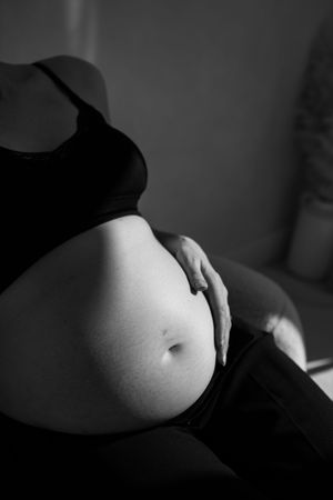 woman sitting with her bump In a spot of sunlight during her maternity session in the studio.