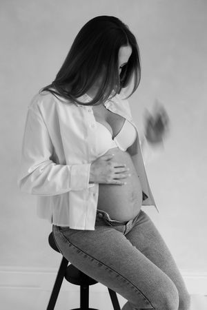 blurry black and white image of woman posing while sitting on a stool playing with her hair during her maternity session