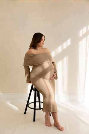 woman sitting on a stool looking out of the window showcasing her bump during a maternity session based in Teeside studio.