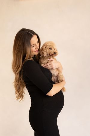 woman holding her cream dog smiling as they bond during her maternity session based in Billingham.