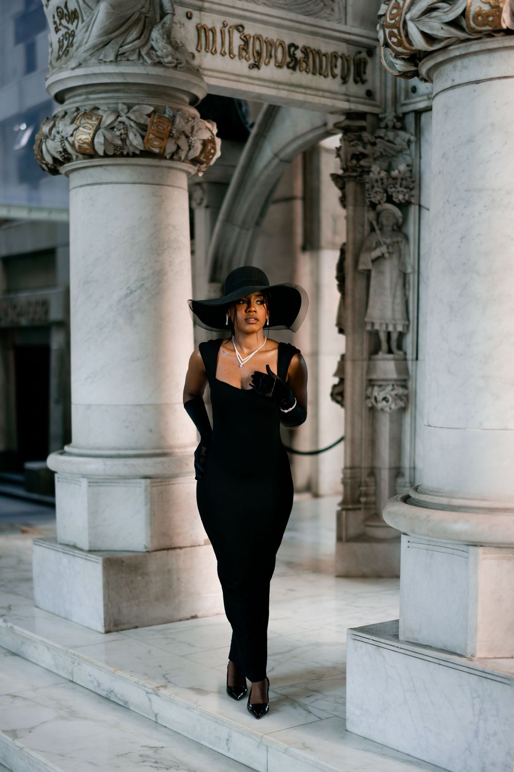 Fashion portrait of woman in black dress walking between ornate stone columns.