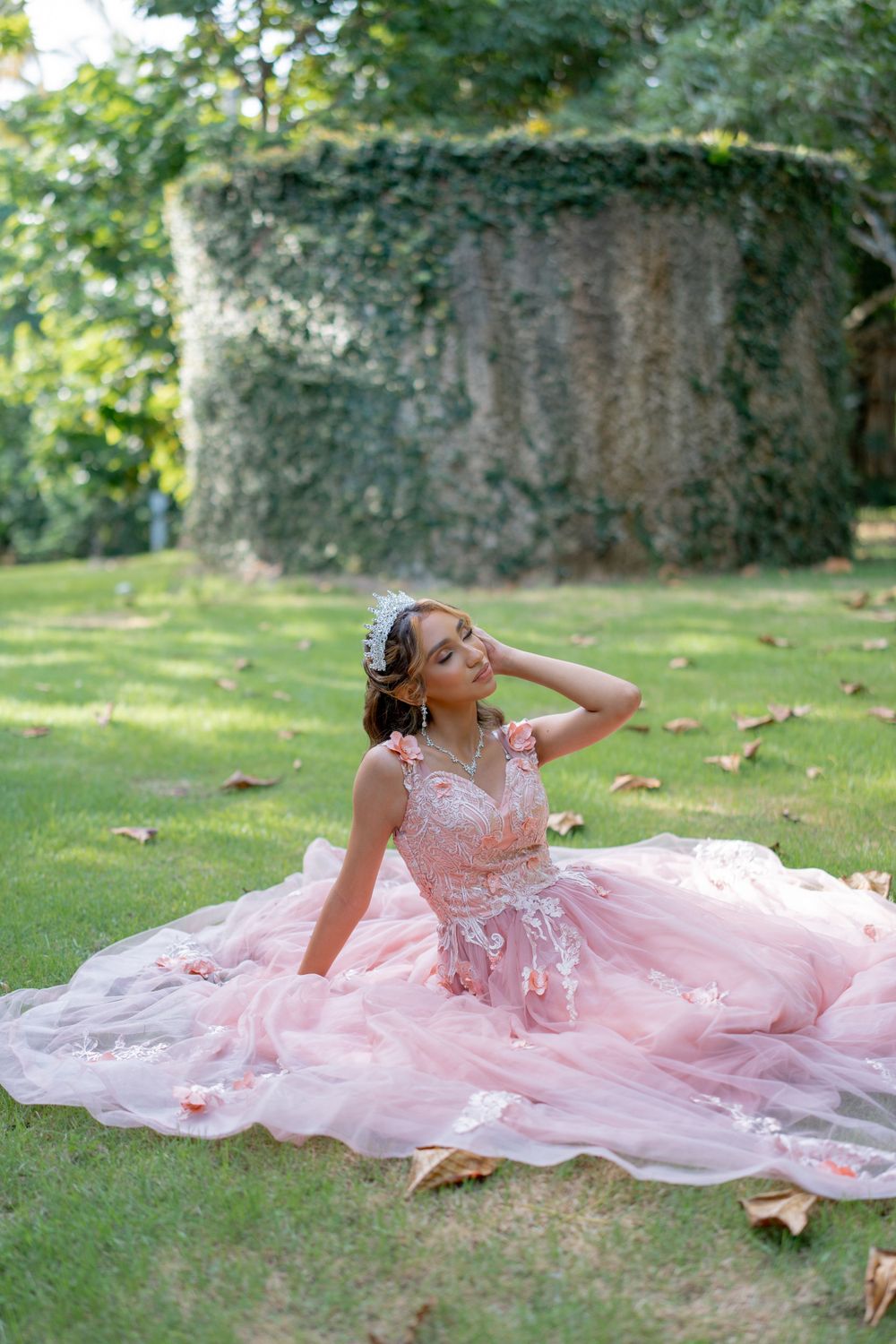 Dreamy photo of someone in a pink princess gown posing on grass near an ivy-covered wall.