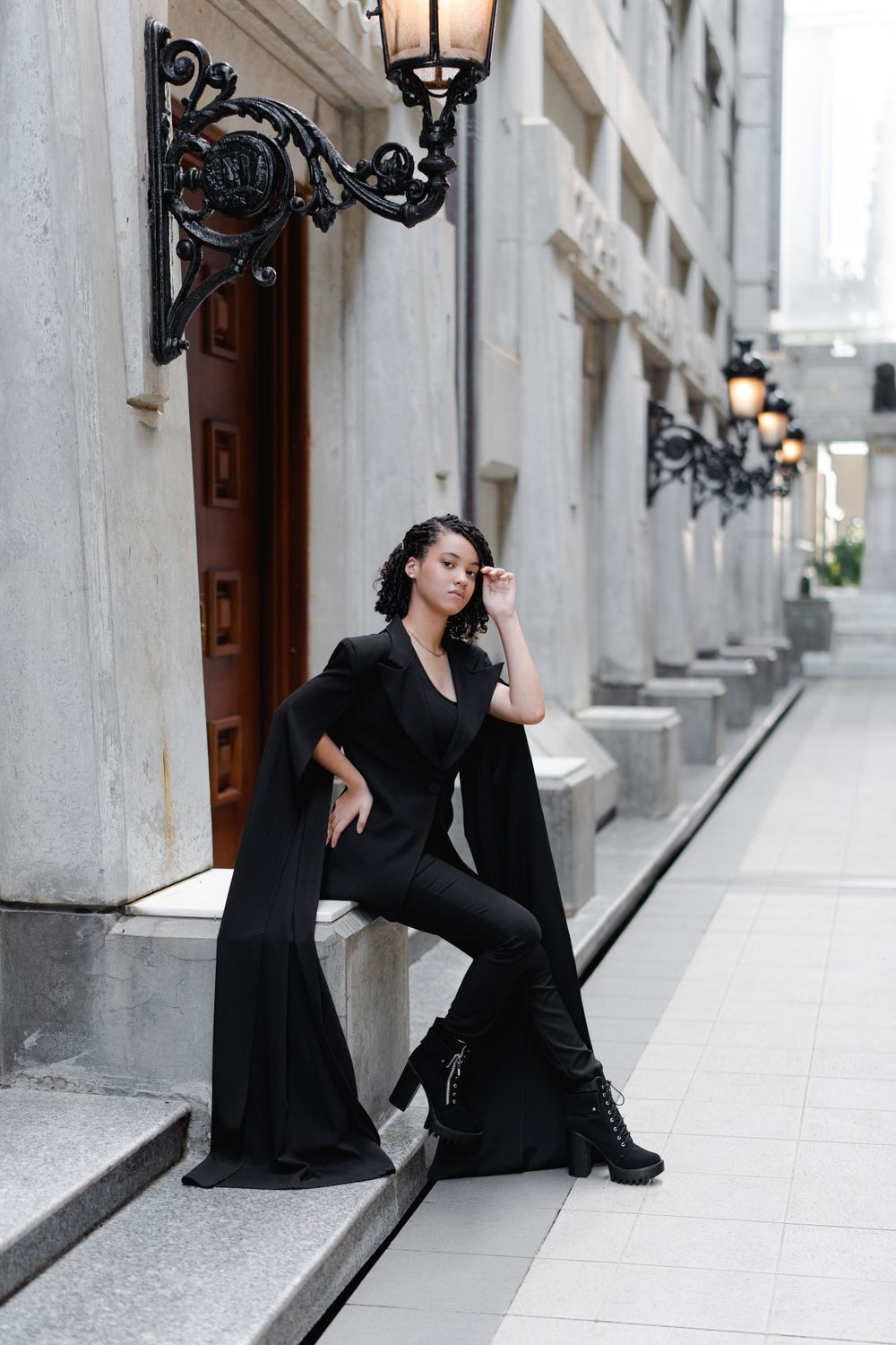Fashion portrait in all black outfit against classic architecture with vintage lanterns.