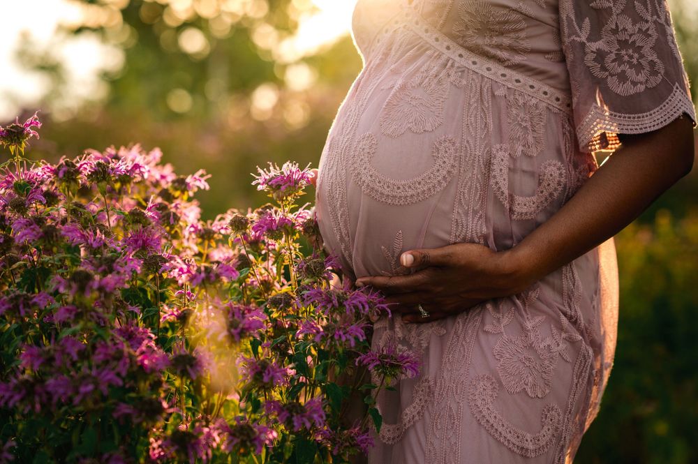 Sunset maternity session with woman in pink dress among blooming flowers.