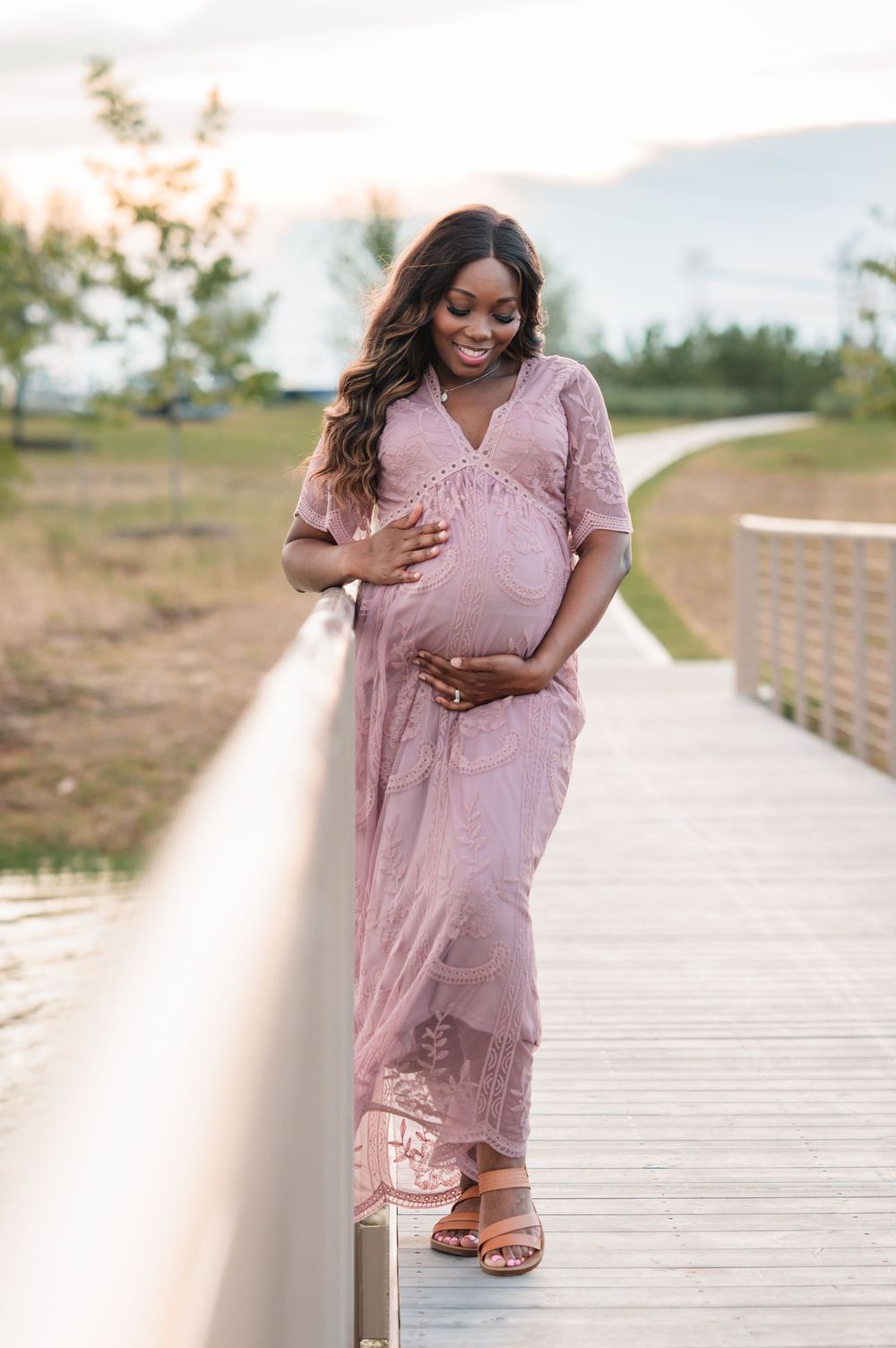 A pink lace dress is worn while walking on a wooden boardwalk during a sunny outdoor photoshoot.