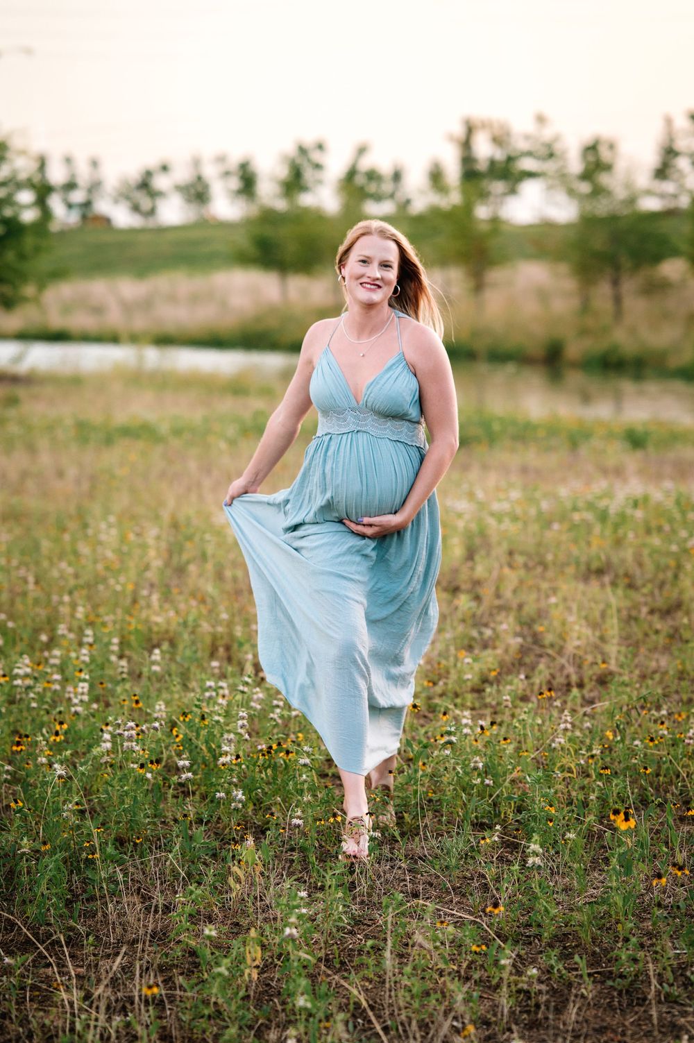 Woman in light blue maternity dress walking through wildflower field.
