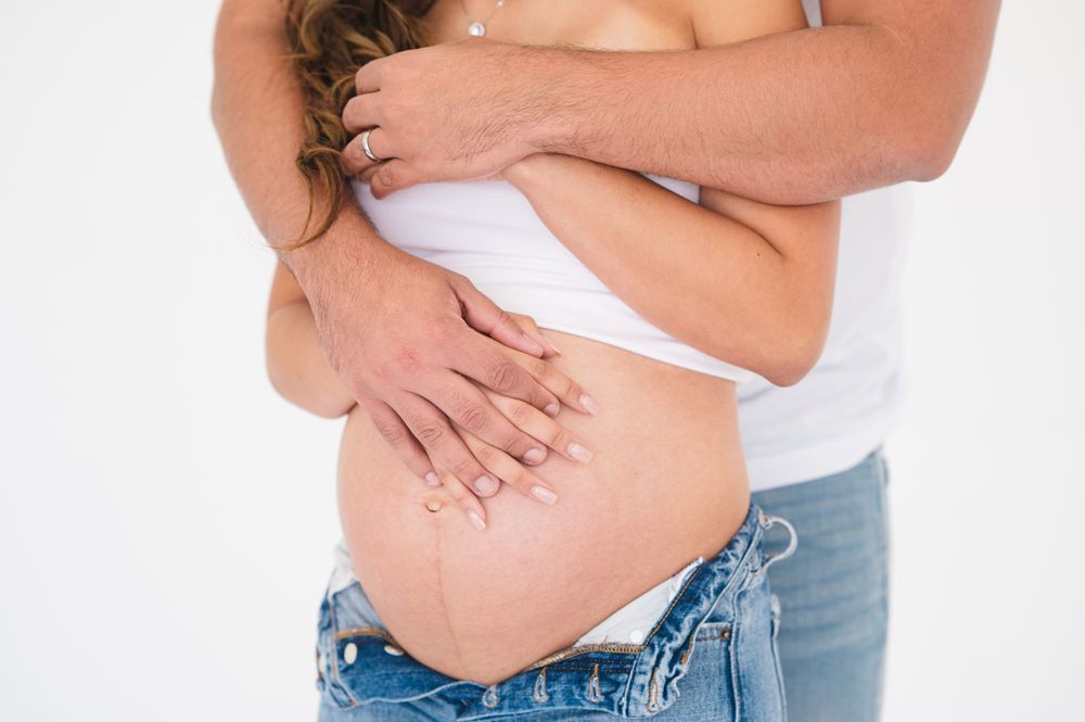 Intimate maternity portrait of couple in white and denim against white backdrop.