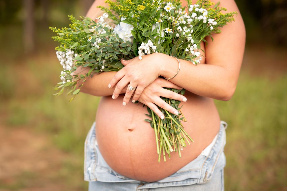 Delicate wildflower bouquet held against a growing baby bump in soft natural light.