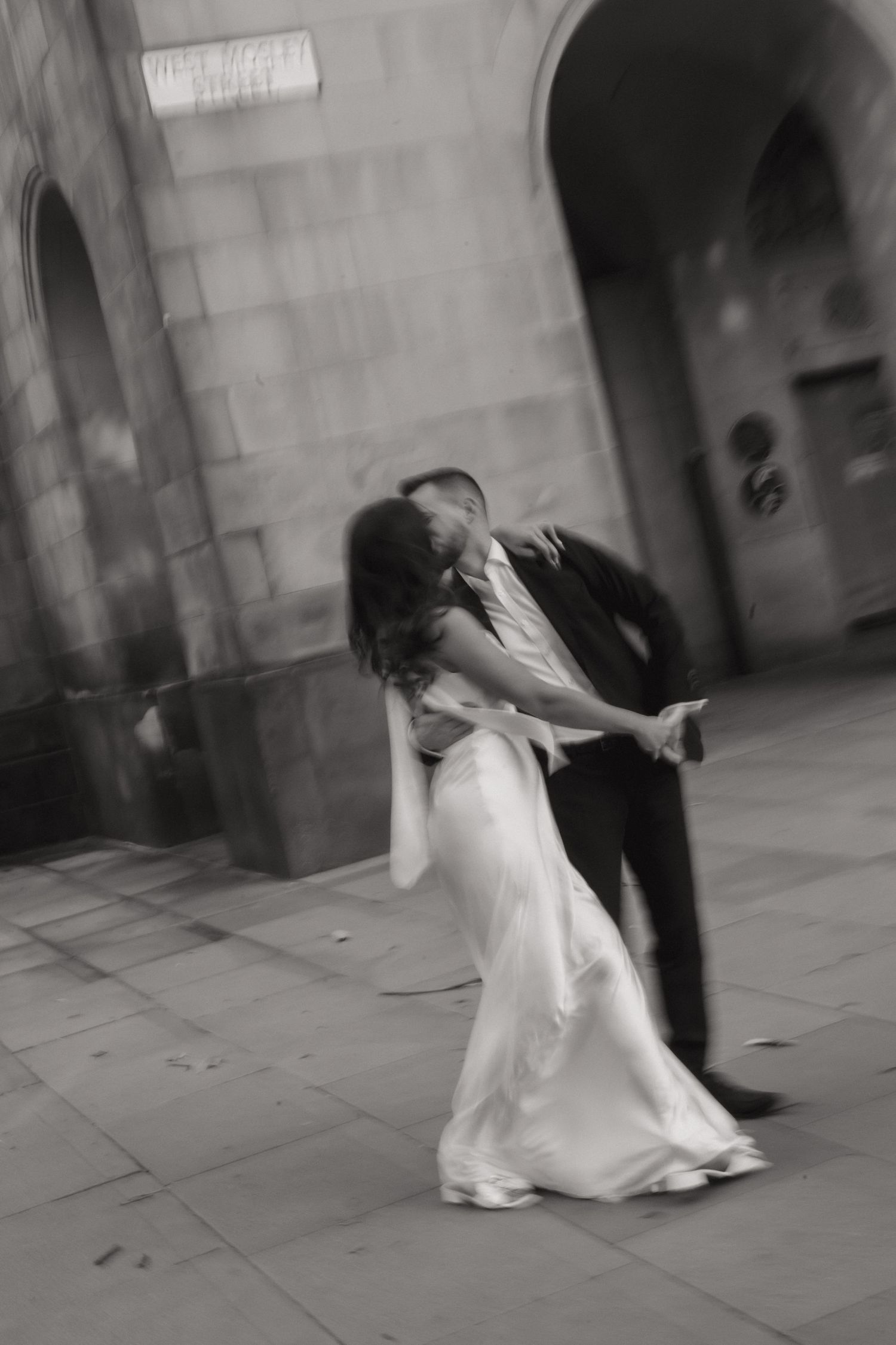 A sequence of black and white photos showing a couple dancing together in an elegant stone hallway.