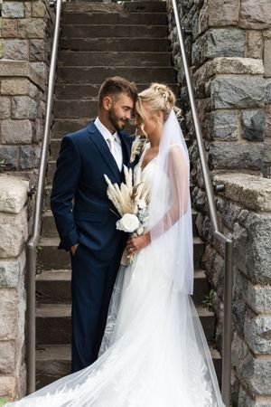 Romantic wedding portrait on stone staircase with couple holding dried flower bouquet.