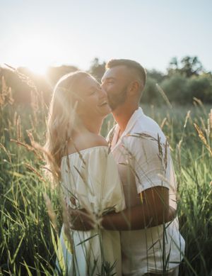 A romantic couple embraces in tall grass during golden hour sunlight.