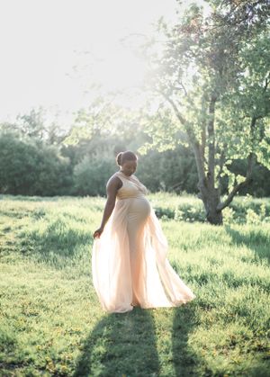 Flowing dress silhouette against sunlit grass and trees in an ethereal outdoor setting.