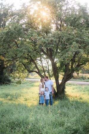 Family walks together through a sunlit field with green trees on a summer evening.