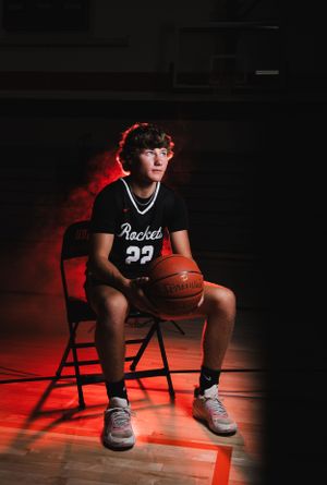 Basketball player in black jersey sits on chair with dramatic red lighting.