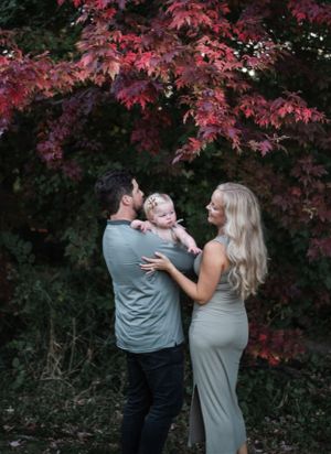 Couple poses playfully under vibrant red autumn maple leaves in outdoor photoshoot.