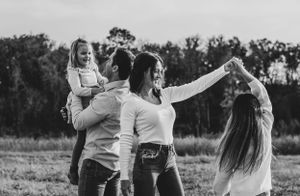 Black and white photo of family dancing together in an open field at sunset.