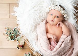 Baby resting on white fur with floral crown and pink wrap.