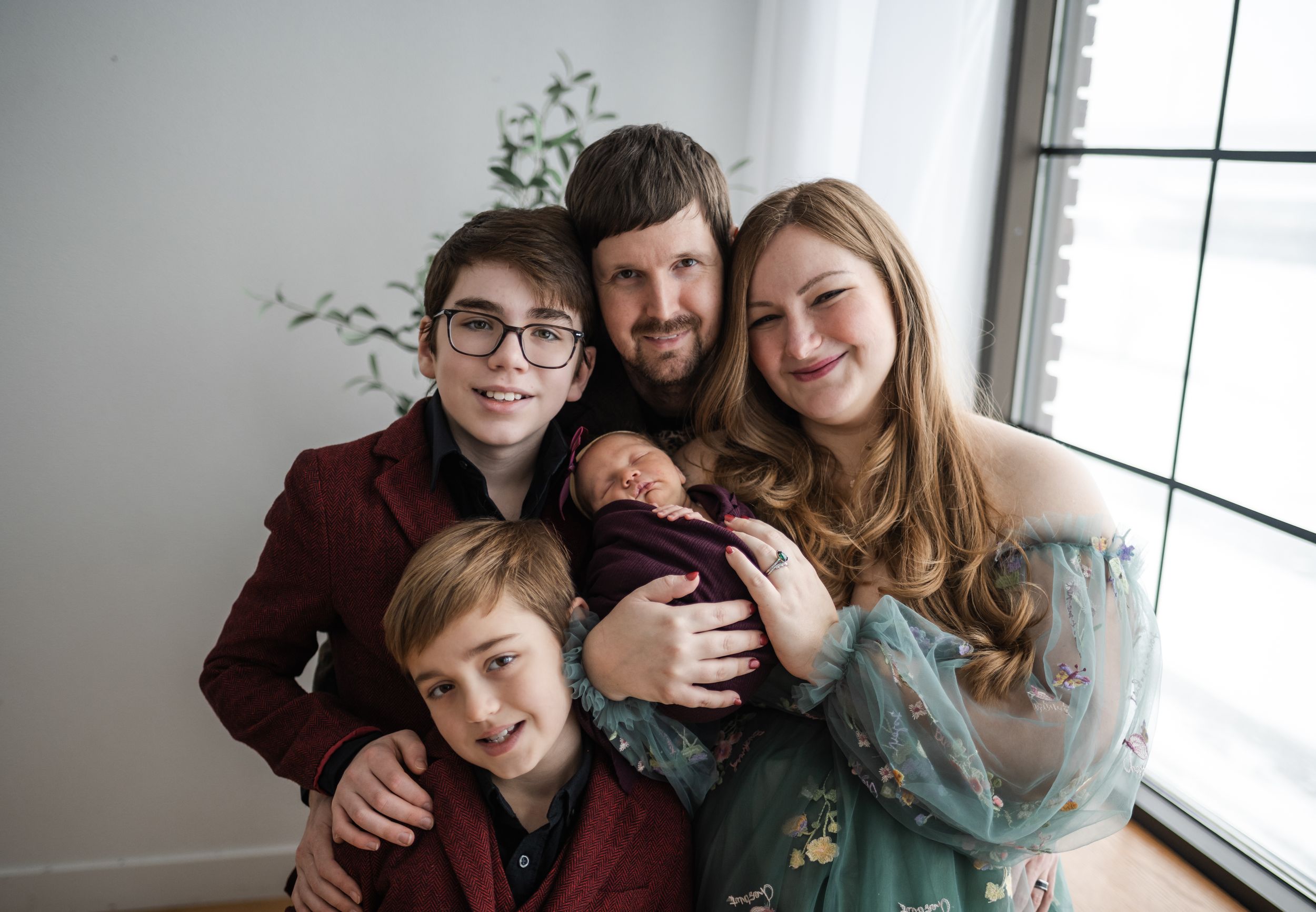 A family group poses together by a bright window in a series of candid lifestyle photos.