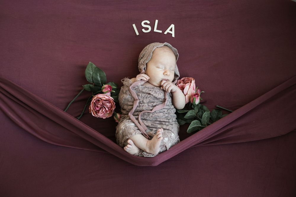 A sleeping baby wrapped in pink fabric lies in a heart-shaped wooden prop during a newborn photography session.