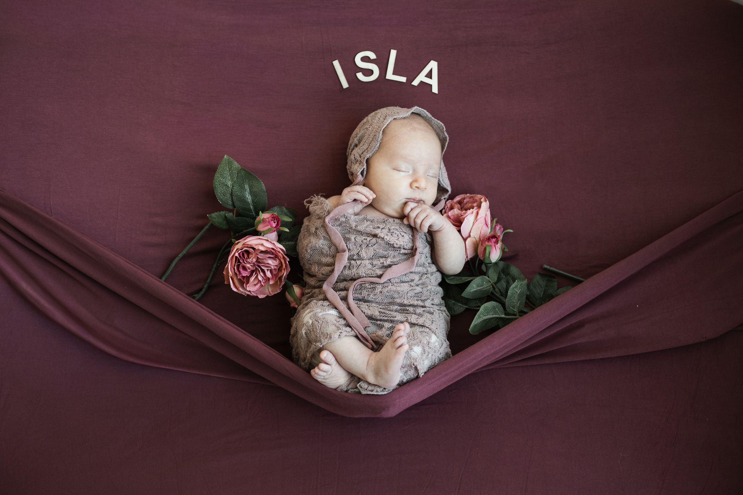 A sleeping baby wrapped in pink fabric lies in a heart-shaped wooden prop during a newborn photography session.